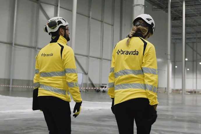 Two technicians wearing high-visibility clothing and safety helmets at a construction site.