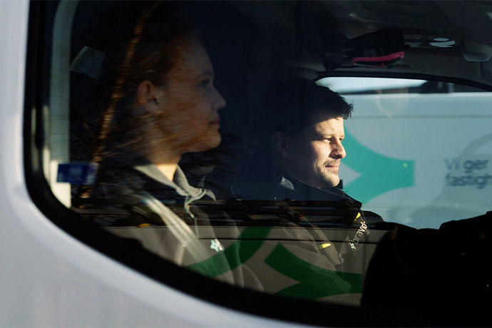 Two people in work clothes are traveling in a service vehicle.
