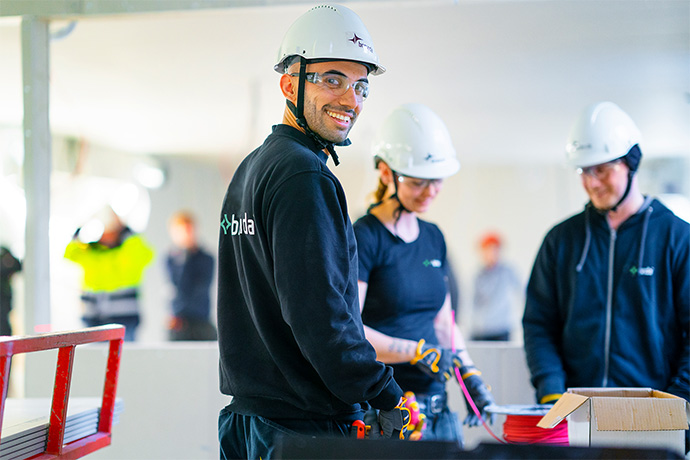Bilden visar personer med skyddsutrustning: Alla på bilden bär säkerhetshjälmar och skyddsglasögon, vilket tyder på att de arbetar i en miljö med höga säkerhetskrav.